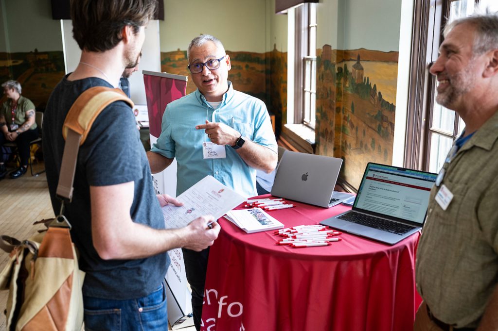 3 men stand at a table talking and smiling.