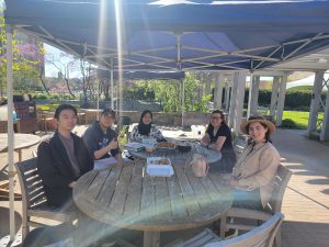 Bacteriology MS Students sit around a table enjoying food.